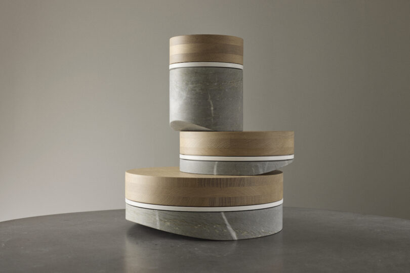 Three cylindrical containers made of stone and wood, stacked in a balanced, off-centered arrangement on a flat surface