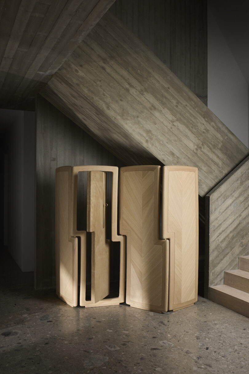 Wooden, geometric folding screen with mirrored surface near a concrete staircase on a stone floor