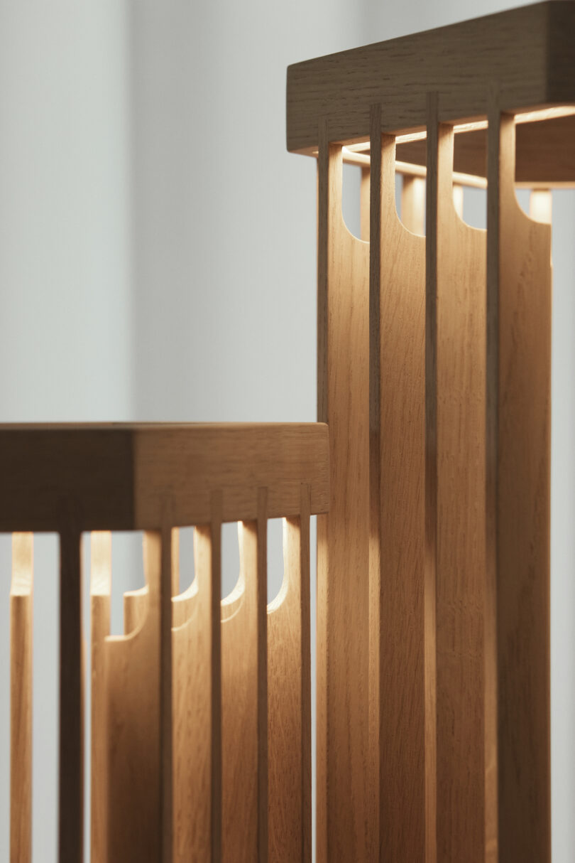 Close-up of two wooden structures with vertical slats, each illuminated from within, casting warm light on the smooth surfaces