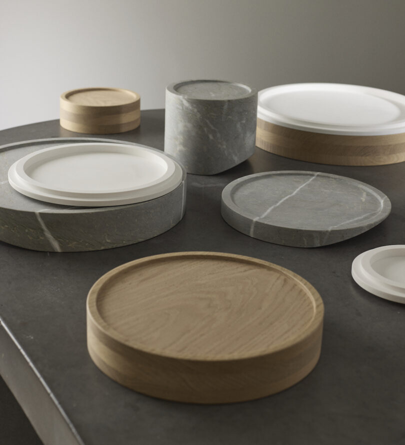A collection of round trays and platters in wood and marble finishes are arranged on a smooth, dark surface