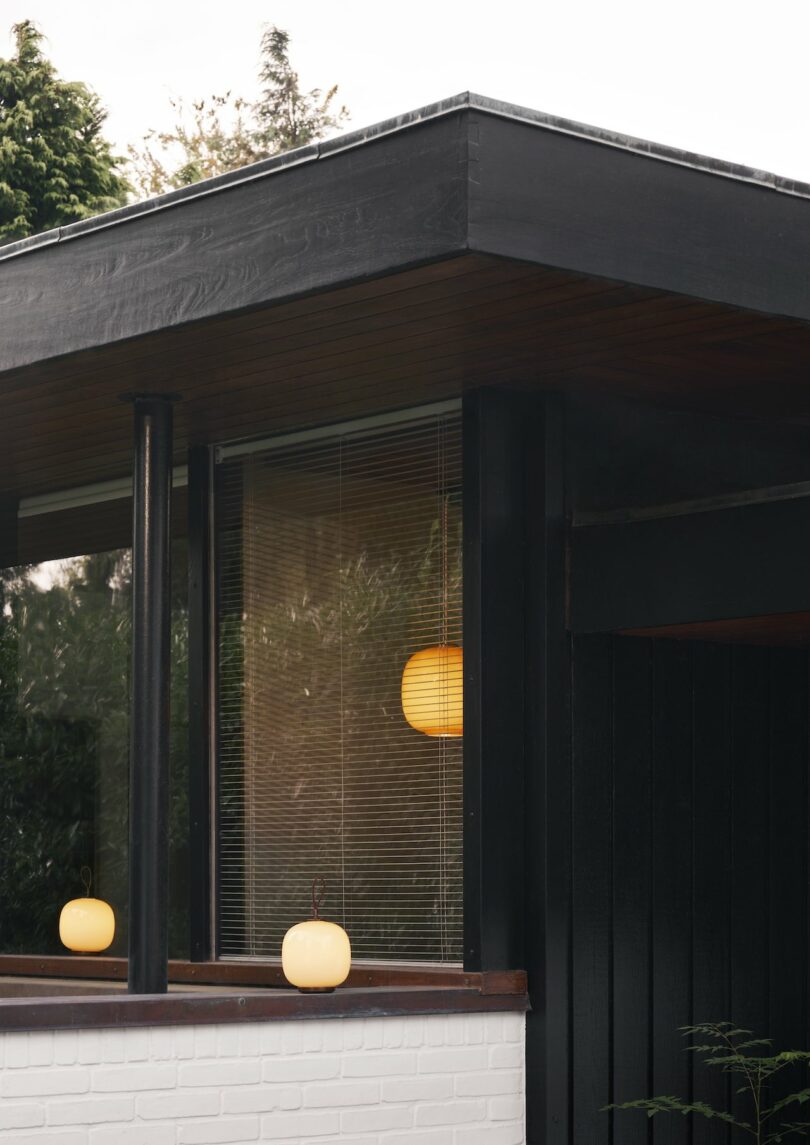 A modern corner of the house features a large window with black trim, where the glow of visible interior and exterior spherical lights harmonizes with the elegant design. Among them, a Louis Poulsen Portable Lamp adds a touch of sophistication to this contemporary setting