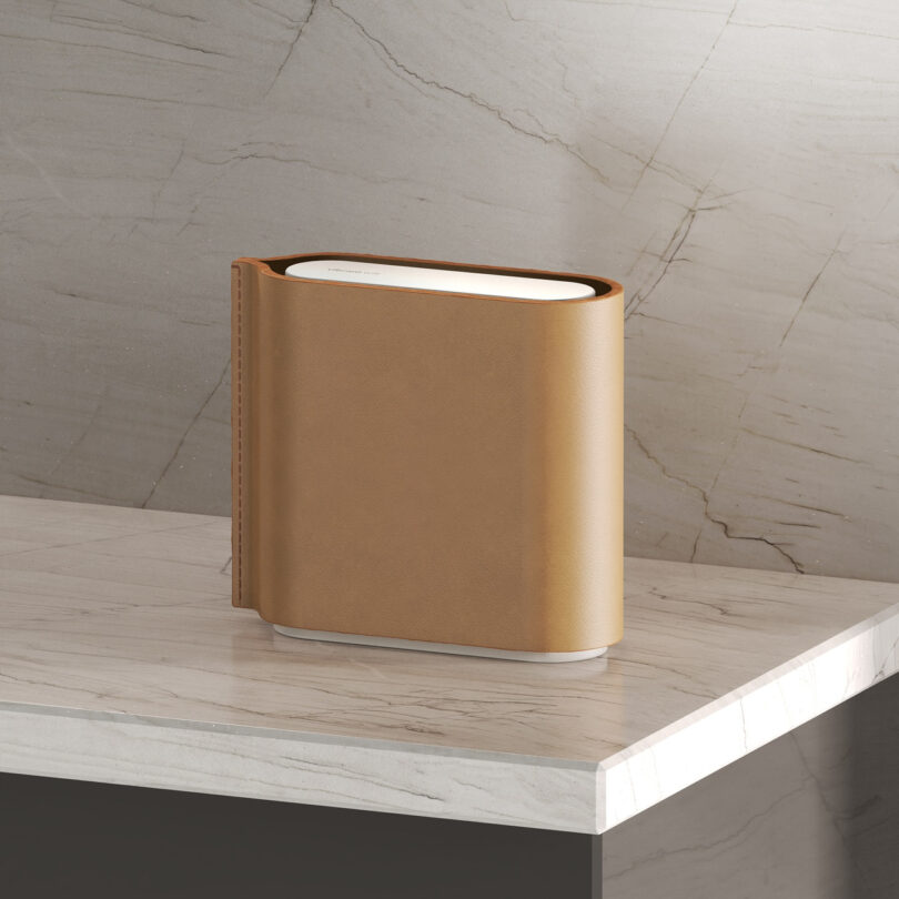 A sleek, modern air purifier with a brown leather-like exterior is placed on a marble surface against a stone-textured wall.