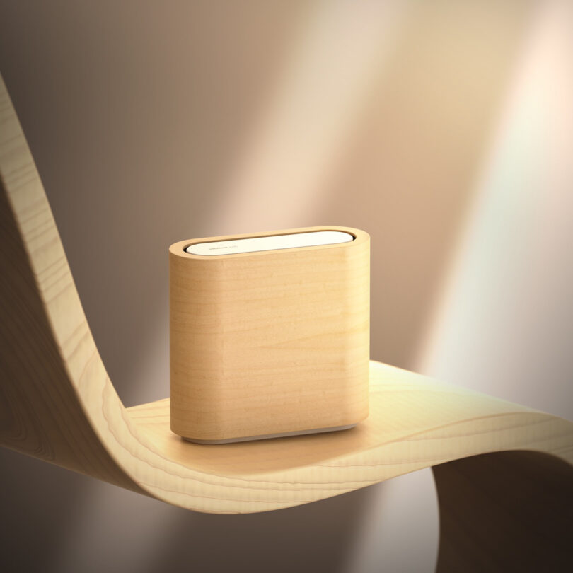 A light wooden, rectangular smart speaker rests on a curved wooden surface, illuminated by soft lighting.