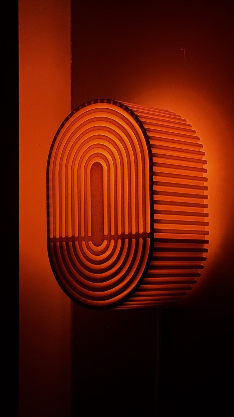 The Walmen red, oval-shaped wall lamp with a grooved, concentric pattern emits a Dumaliang warm glow against a dark background