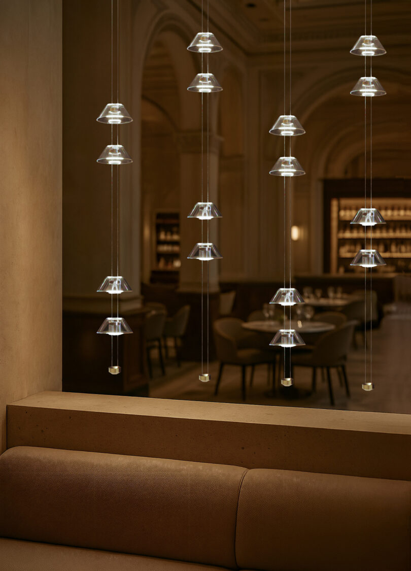 Aura pendant lights with glass shades hang in vertical rows above a seating area in a dimly lit, modern interior space with arched architectural details.
