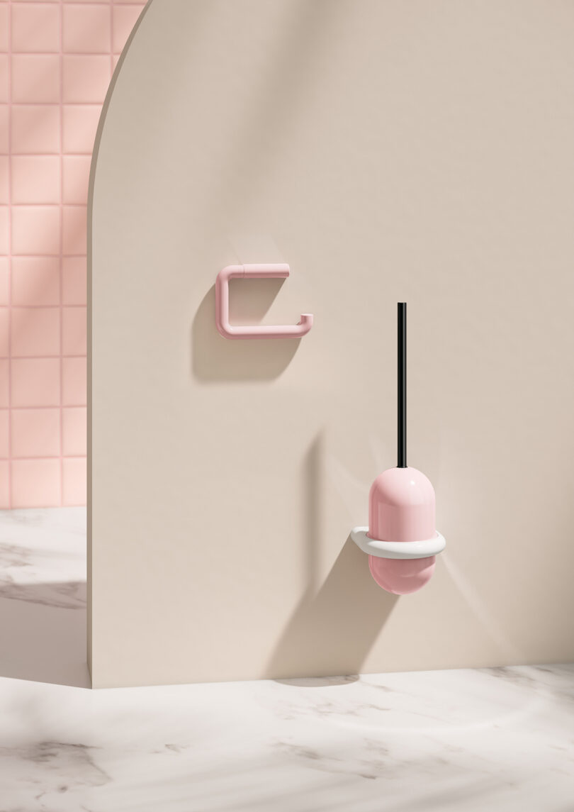 A minimal bathroom scene featuring a pink toilet brush in a holder and an empty pink toilet paper holder mounted on a beige partition wall with marble flooring.