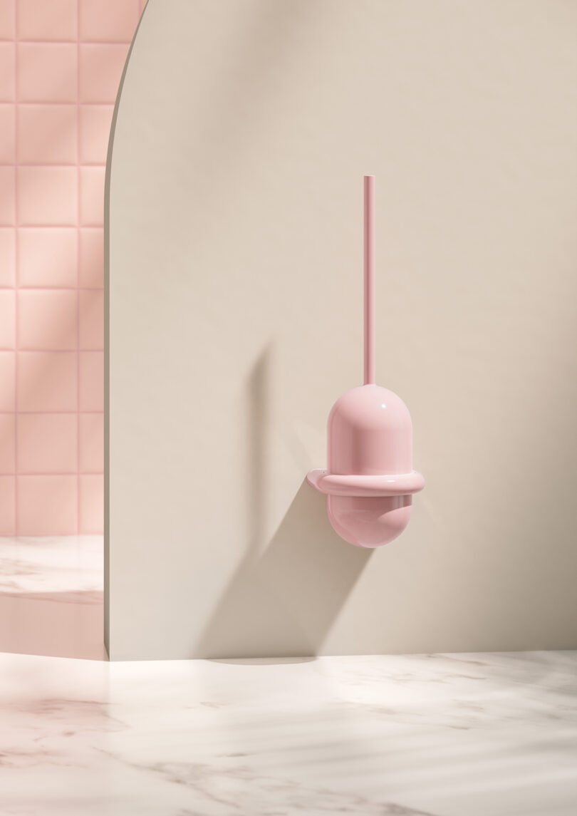 A pink toilet brush with a holder mounted on a light-colored wall in a bathroom with pink tiles and a marble floor.