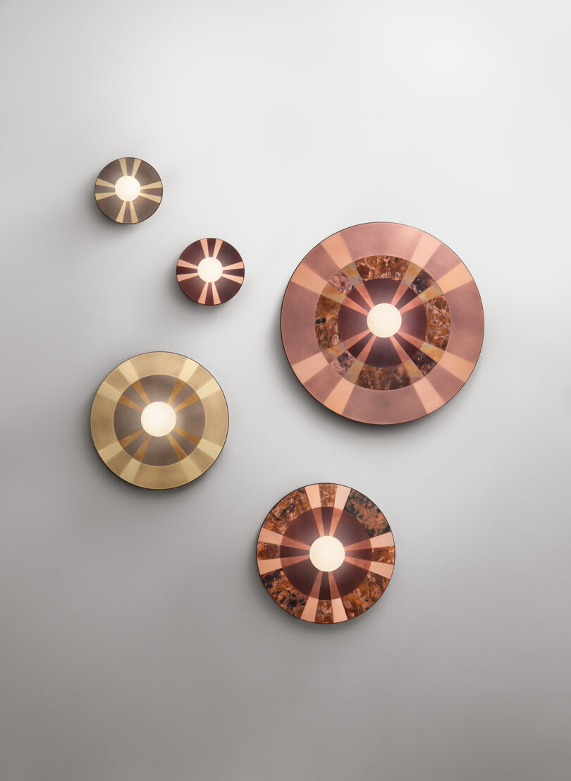 Five circular wall lights with radial patterns on a light gray wall, displayed in an asymmetrical arrangement.