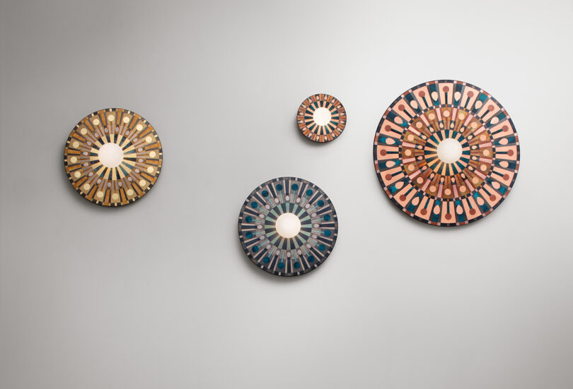 Four round, decorative wall mirrors arranged in a pattern on a plain white wall. Each mirror features intricate, colorful designs with a central reflective surface.