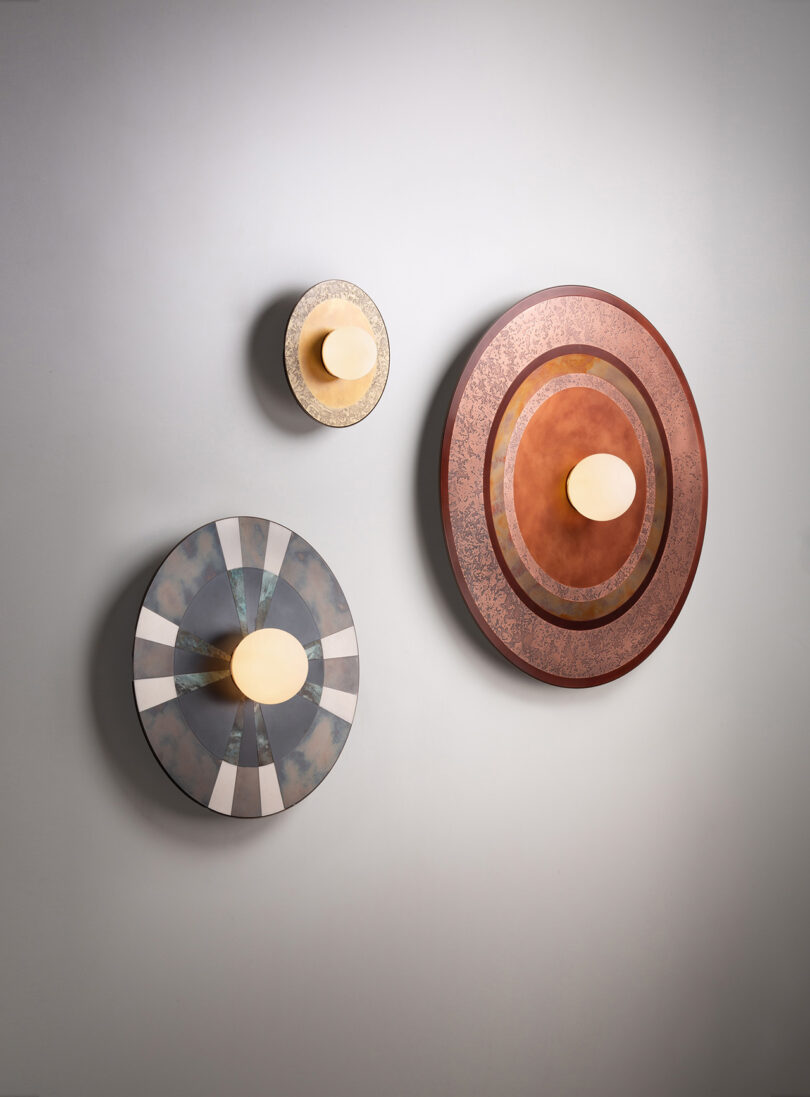 Three circular wall lights of varying sizes with geometric designs and central bulb fixtures mounted on a gray wall.