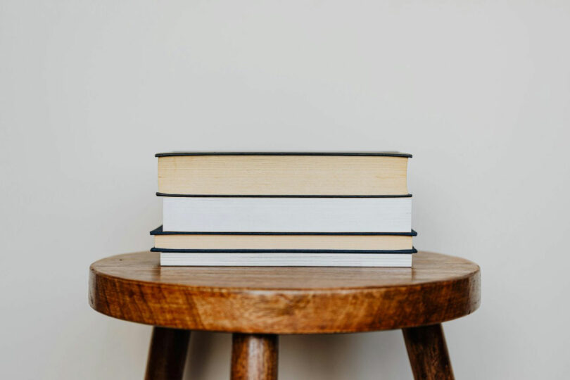 Three hardcover books, penned by Elizabeth Rees, are stacked on a wooden stool against a plain white background.