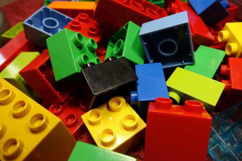 A pile of assorted colorful plastic building blocks, including red, yellow, green, blue, and black pieces, reminiscent of Katherine Duclos's vibrant artistic palette.