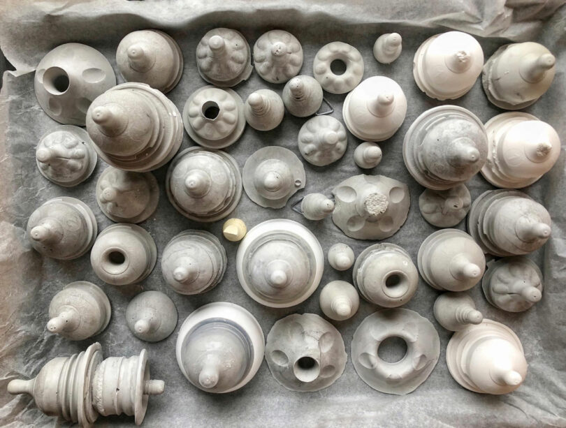 Collection of various gray and white clay objects by Katherine Duclos, featuring conical and cylindrical shapes, arranged on a parchment-lined surface.