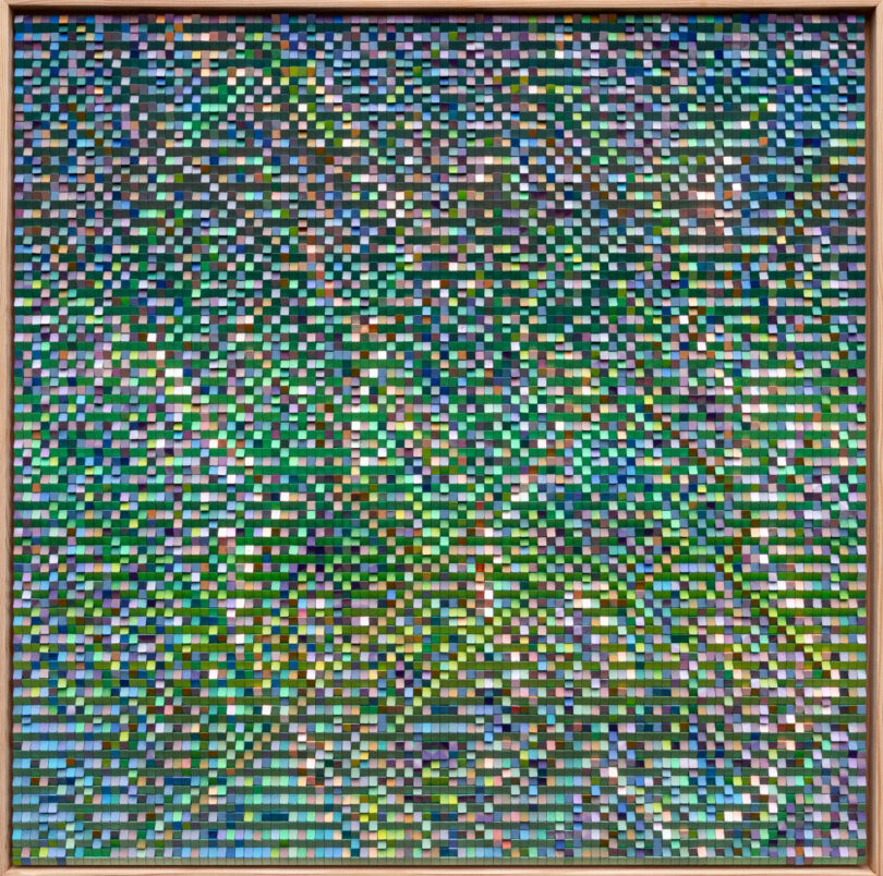 A framed artwork by Katherine Duclos composed of hundreds of small, multicolored rectangular tiles arranged in a grid, creating a mosaic with dominant green, blue, and purple tones.
