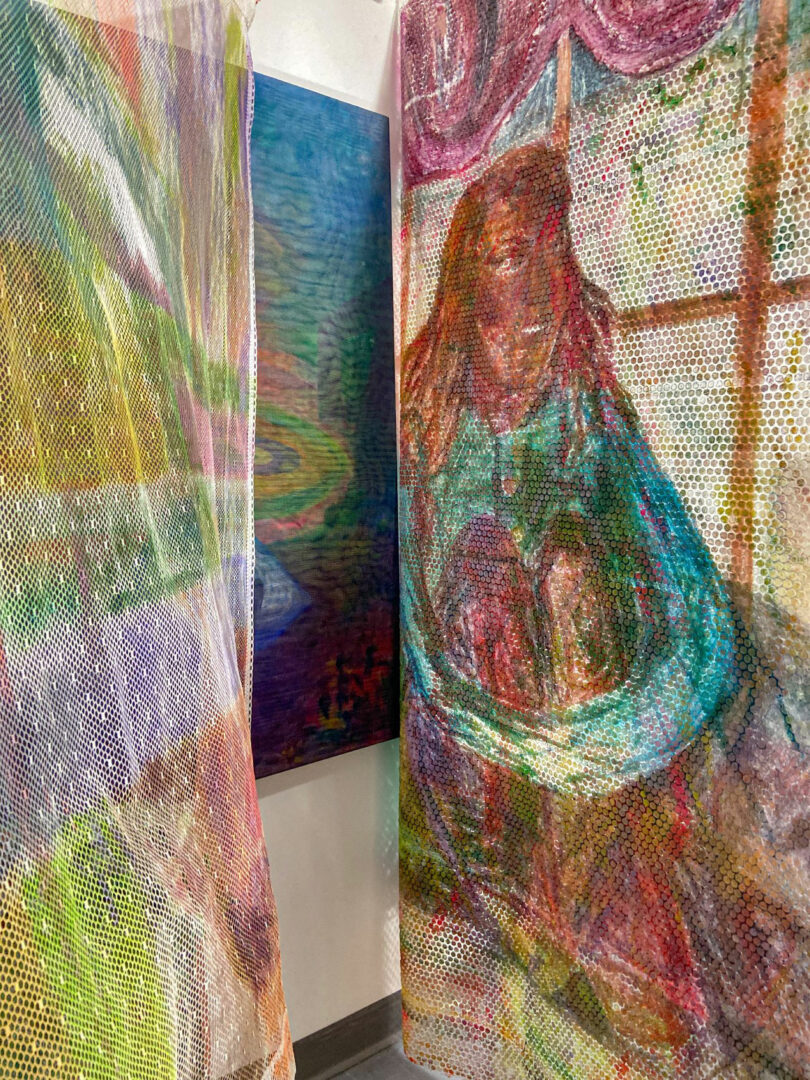 A colorful mesh curtain with a painted figure, created by Katherine Duclos, sits near a window, while another abstract landscape painting hangs on the adjacent wall.