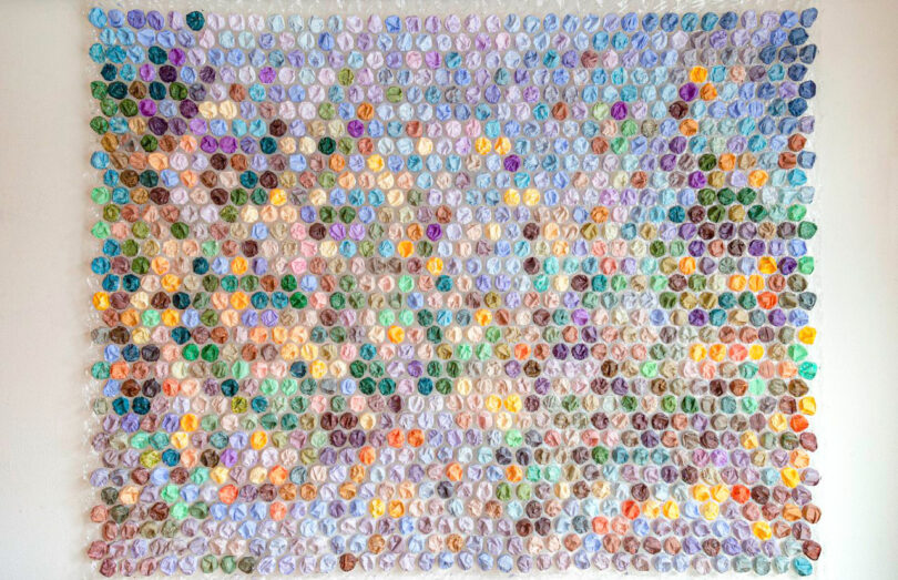A large wall display by Katherine Duclos features many small, multicolored circles arranged in a grid pattern, each circle appearing textured or slightly three-dimensional.