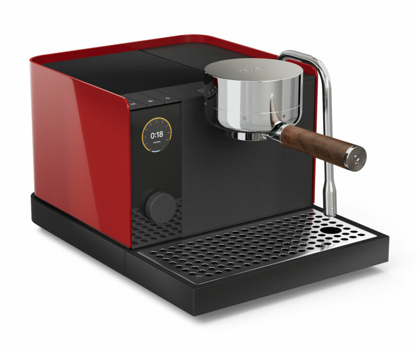 A modern red and black Fellow espresso machine with a digital display, wooden-handled portafilter, and metal steam wand, placed on a drip tray.