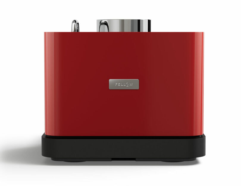 A Fellow red, rectangular toaster with two slots and a metallic accent on top, standing on a black base against a white background.