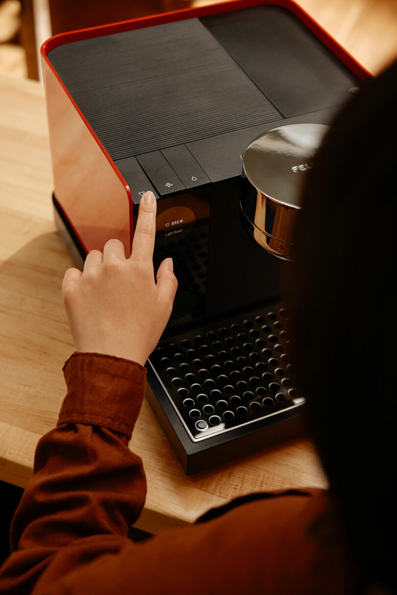 A person presses a button on a sleek Fellow coffee machine placed on a wooden countertop.