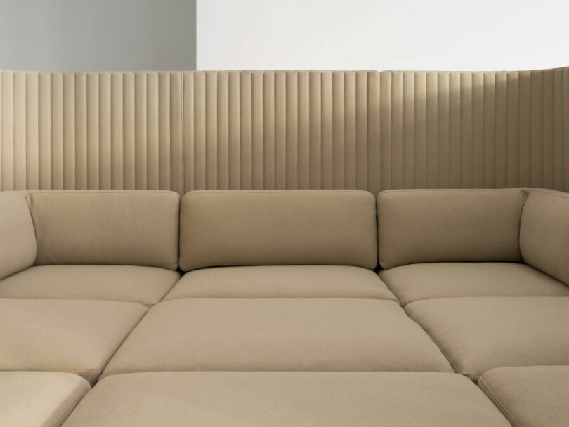 A beige modular sofa with a high, vertically ribbed backrest against a plain light-colored wall.