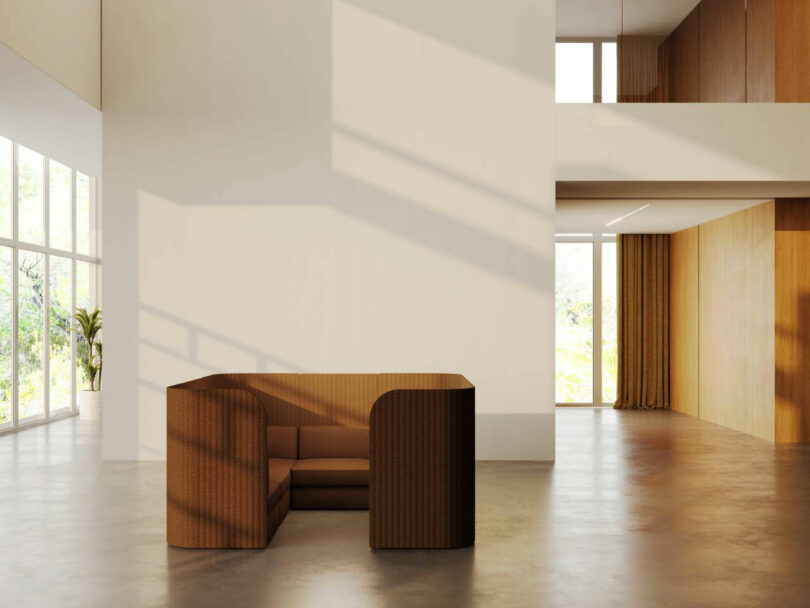 A modern minimalist room with a brown, curved sofa set against a white wall, large windows, concrete floor, and wooden accents.