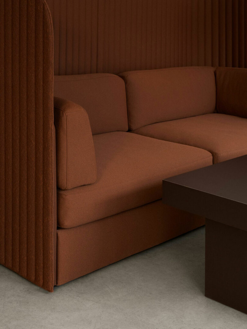 Brown upholstered sectional sofa with tall ribbed side panel next to a dark brown rectangular coffee table on a light-colored floor.