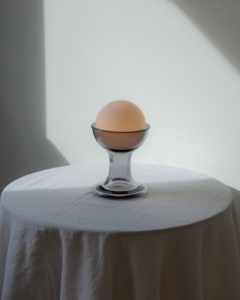 A frosted glass sphere sits on a clear glass stand atop a round table covered with a white cloth, illuminated by sunlight from the side.