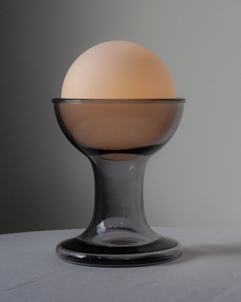A frosted glass sphere is placed inside a clear glass goblet on a white surface against a plain background.