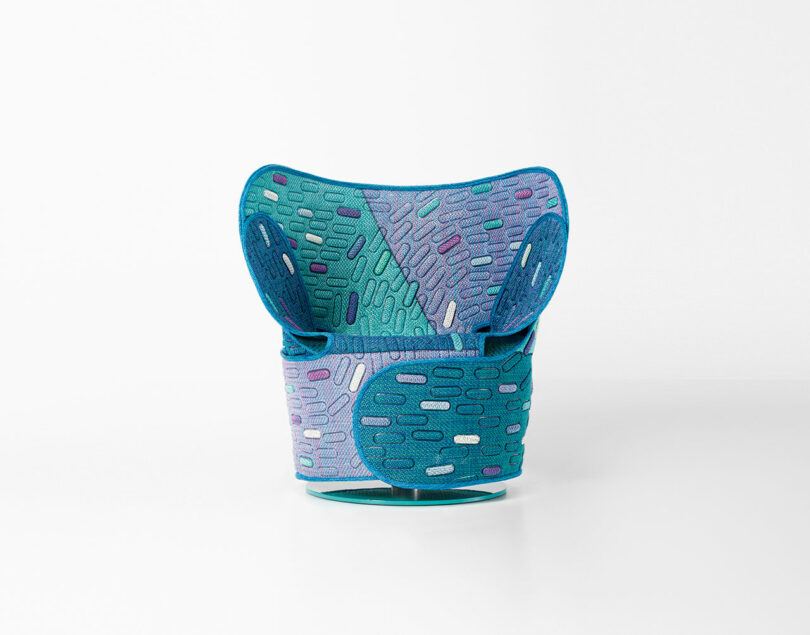 A modern, sculptural chair with a patchwork design in shades of blue, teal, and purple on a white background.