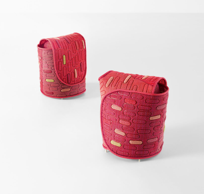 Two red, textured fabric containers with a flap design and abstract patterns, placed on a white surface.