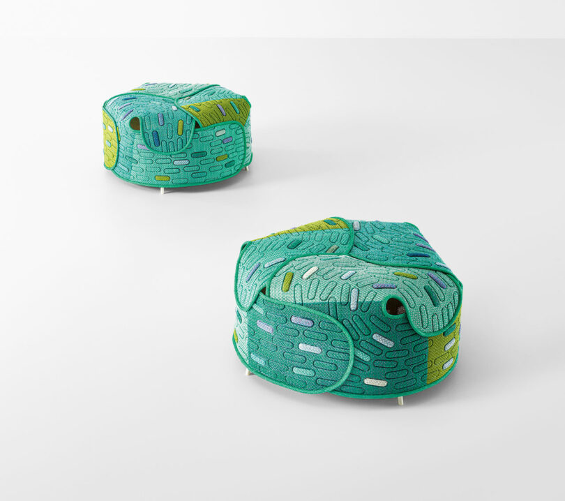 Two green, hexagonal fabric ottomans with textured, abstract patterns sit on a plain white surface.
