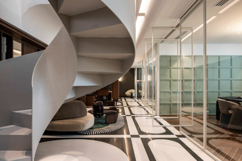 A modern interior features a white spiral staircase, geometric black and white flooring, glass partition walls, and contemporary furniture in a neutral color palette.
