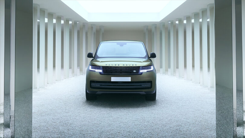 A green Range Rover is parked front-facing in a minimalist, column-lined space with white gravel and a skylight above.
