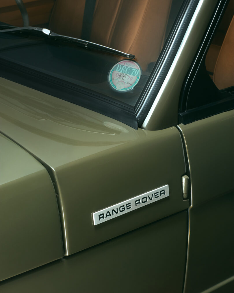 Close-up of a green Range Rover showing the vehicle’s badge on the side panel and part of the windshield with a tax disc displayed.