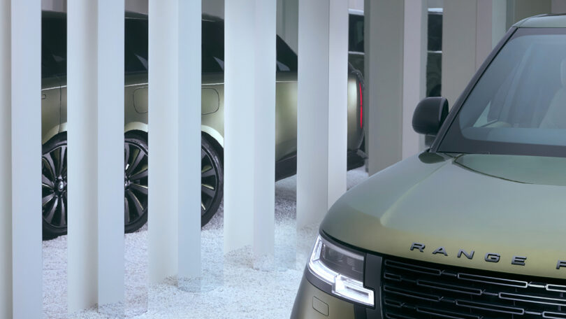 A green Range Rover is partially visible behind vertical frosted glass panels, with gravel on the ground.