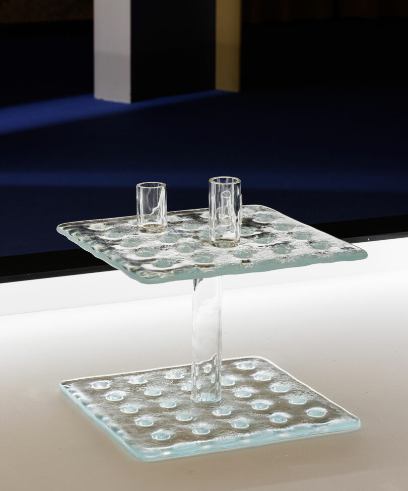 A modern POETICA Wonderglass side table with two square, textured surfaces and two clear glass cups on the top surface, set against a minimal indoor background.