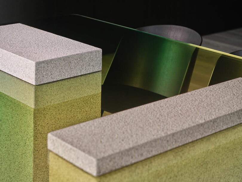 Two rectangular stone slabs rest on a glossy, gradient-colored table with green and yellow hues; black chairs are visible in the background.