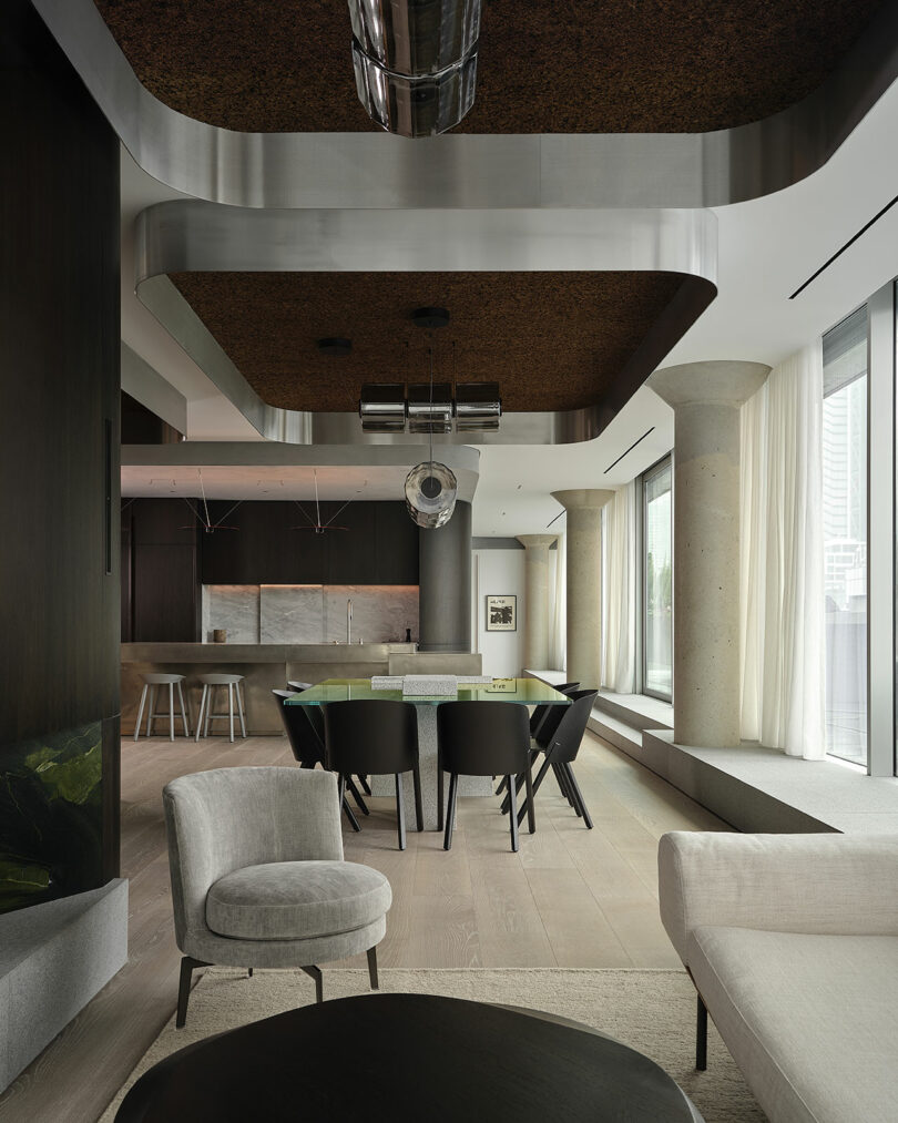 Modern open-plan living and dining area with neutral tones, contemporary furniture, large windows, and a minimalist kitchen in the background.