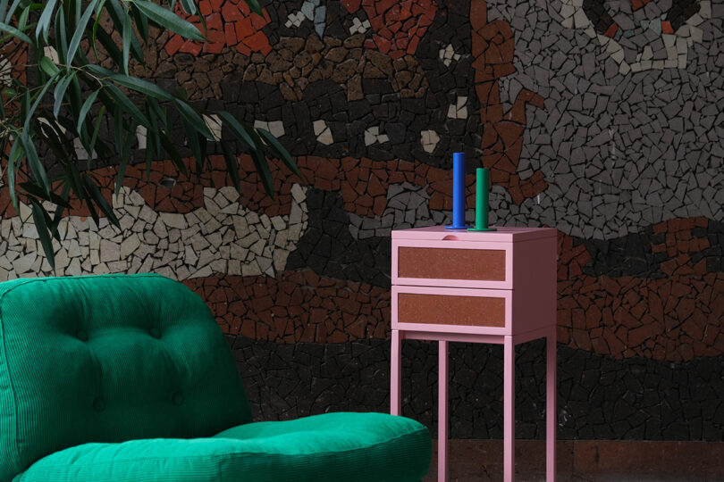 Green chair and pink side table with candles against a mosaic wall.