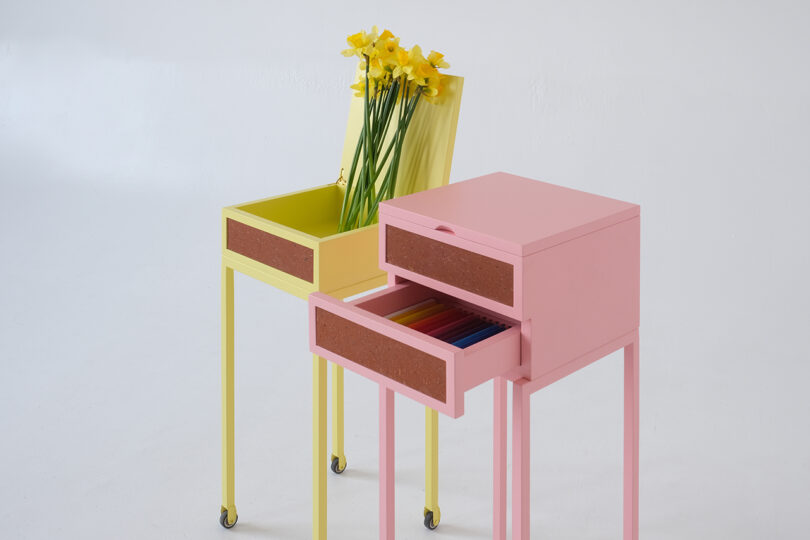 Two tall cabinets on wheels stand against a white background. The yellow cabinet contains daffodils, and the pink cabinet has an open drawer with colorful folders.