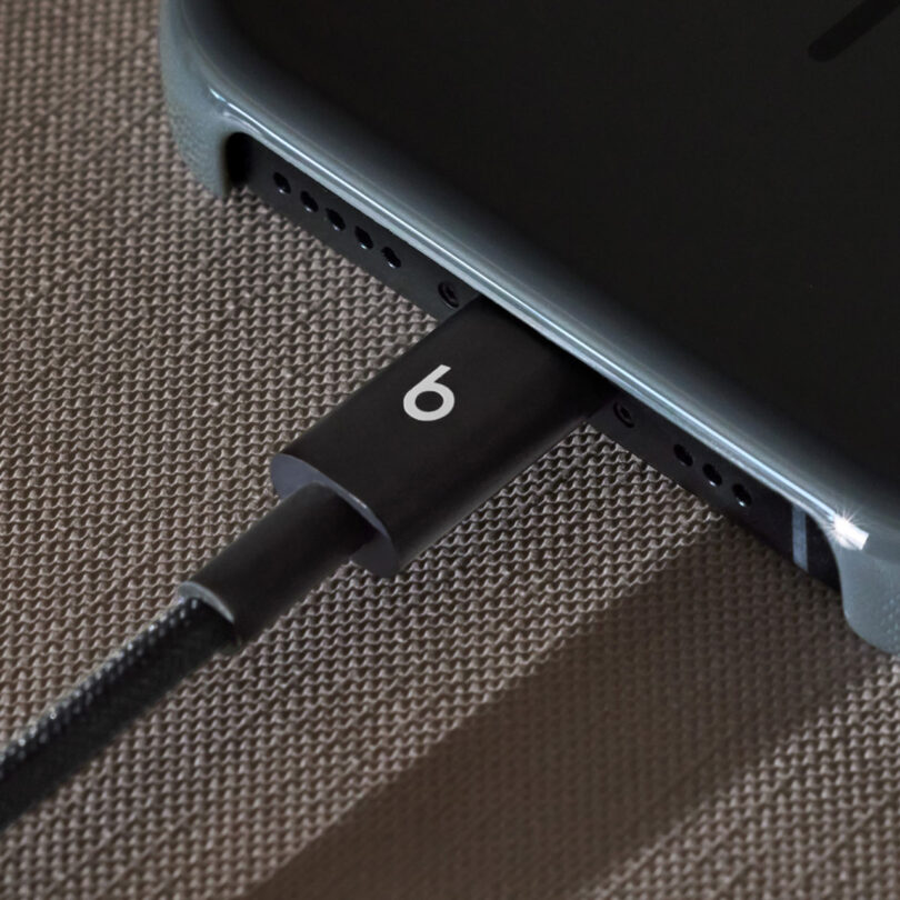 A close-up of a black Beats charging cable plugged into a smartphone on a textured surface.