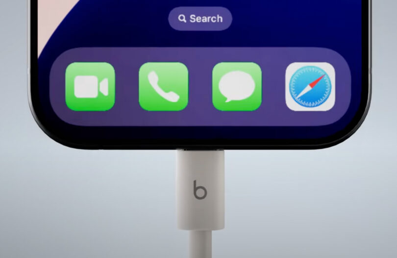 Close-up of the bottom half of a smartphone screen showing app icons, with a charging cable plugged into the device and the Beats app icon visible among the others.
