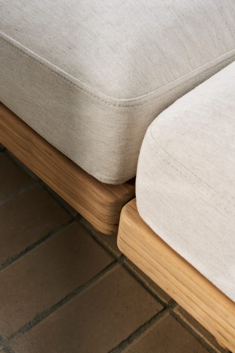 Close-up of two beige fabric cushions on wooden bases, placed on a brick floor