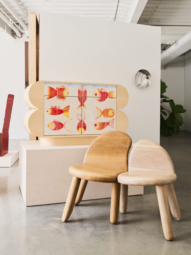 Two wooden chairs with rounded backs are placed in front of a wooden cabinet featuring a colorful fish pattern in a modern, minimalist interior space
