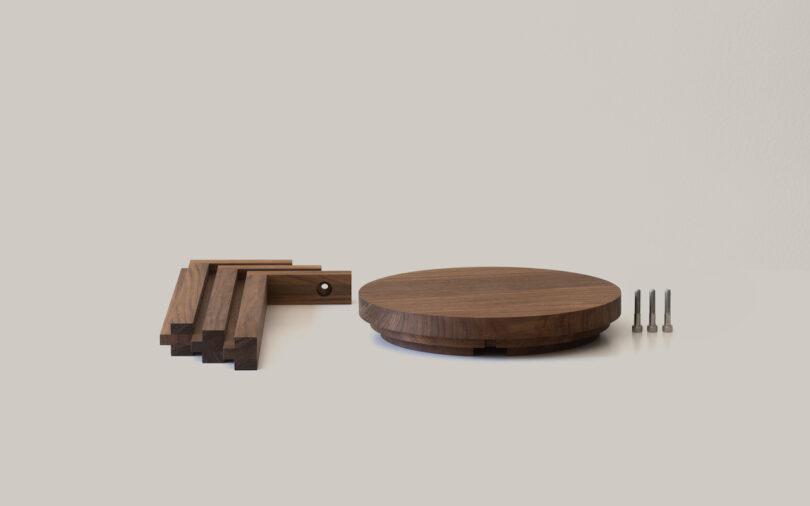Wooden table components on display, including four legs, a circular tabletop, and three screws, against a plain background