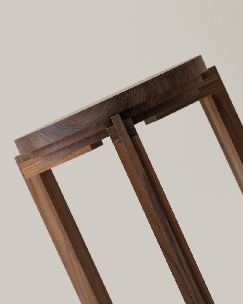 Close-up of a wooden table featuring a round top and angled, decorative legs, set against a plain, light background