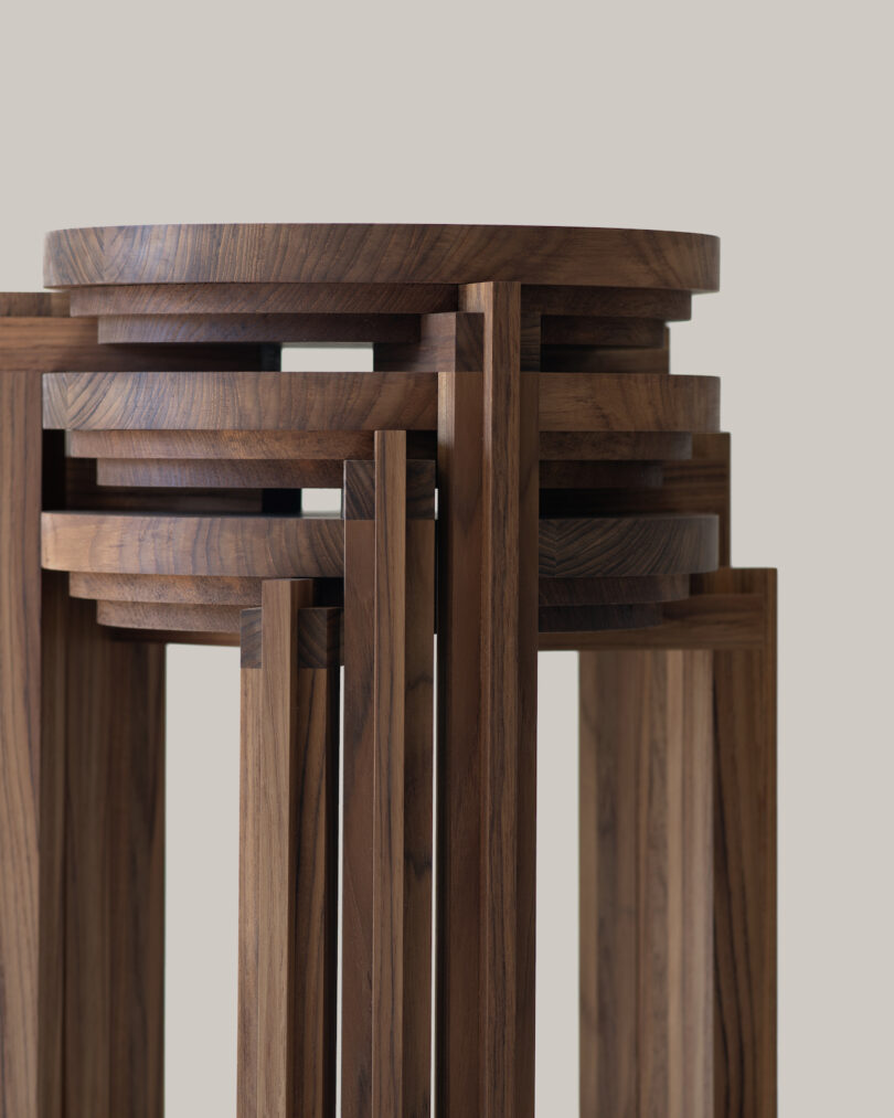 A modern wooden stool with a geometric design, featuring interlocking circular and linear elements. The wood has a rich, natural finish