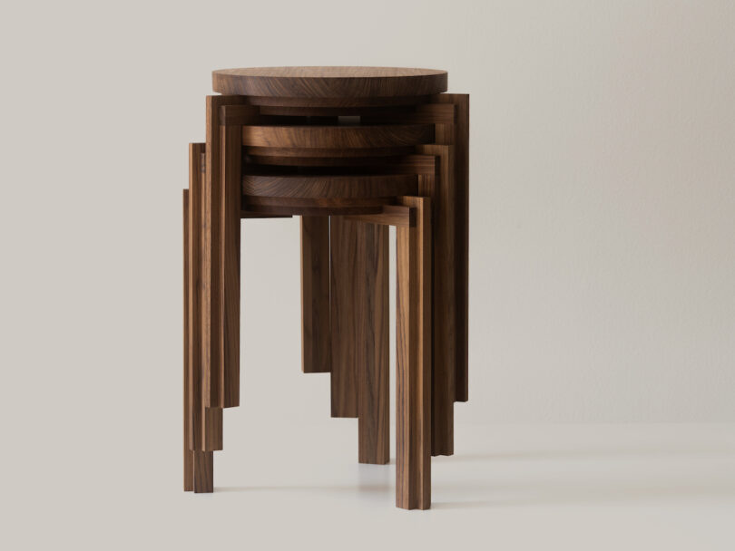 Three wooden nesting stools stacked together on a light surface, showcasing a minimalist design with round tops and angular legs