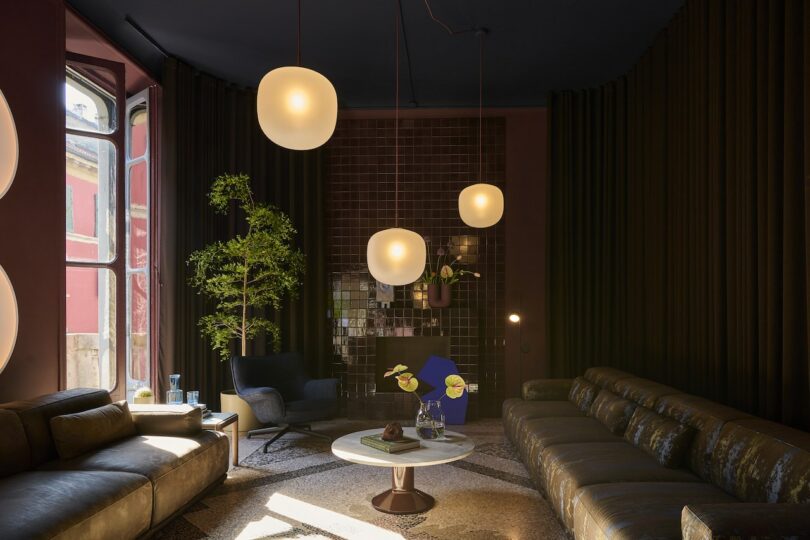 Modern living room with dark walls, large sofas, a round coffee table, potted plant, armchair, and three spherical pendant lights hanging from the ceiling
