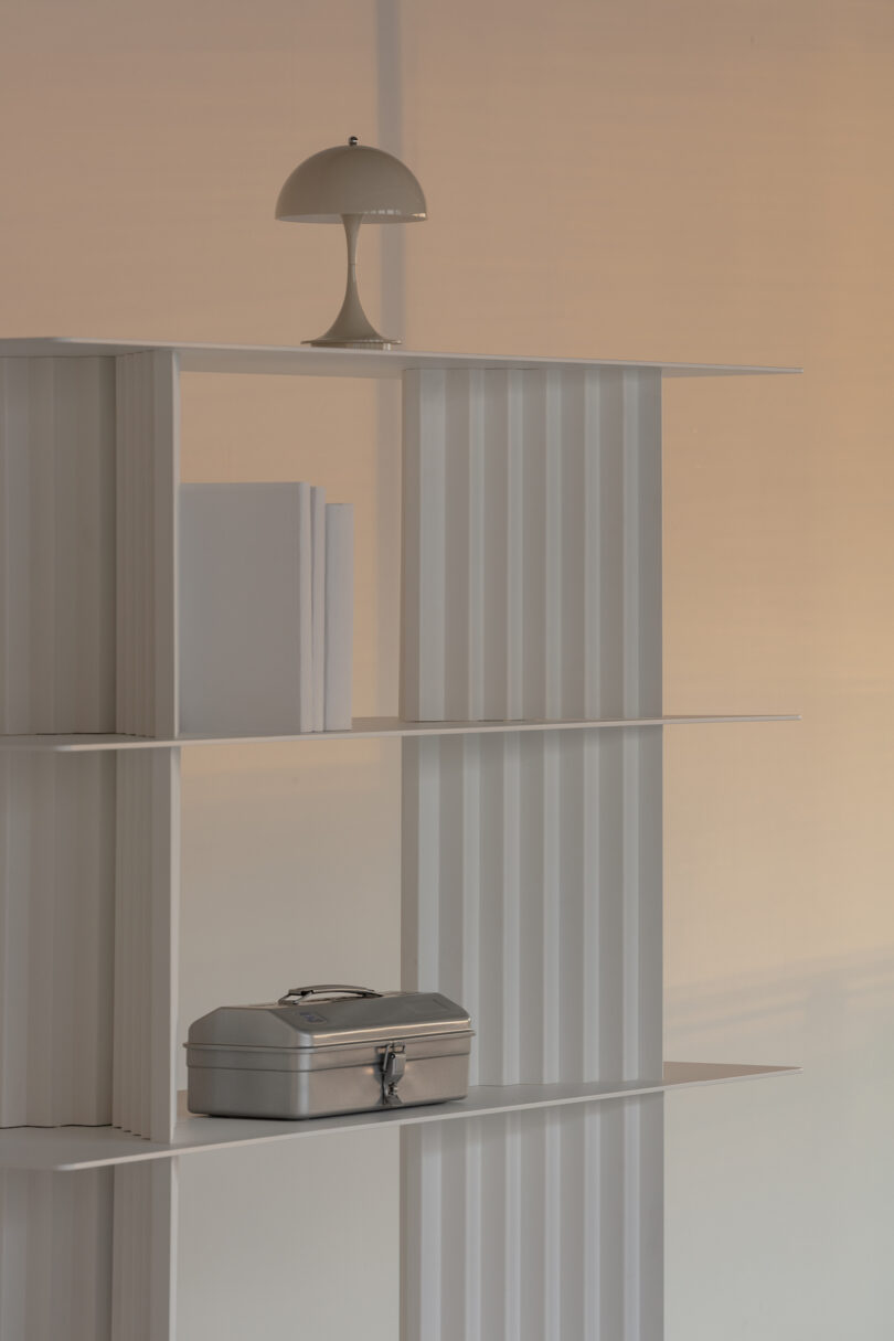 A minimalist white shelf with a lamp, books, and a silver box